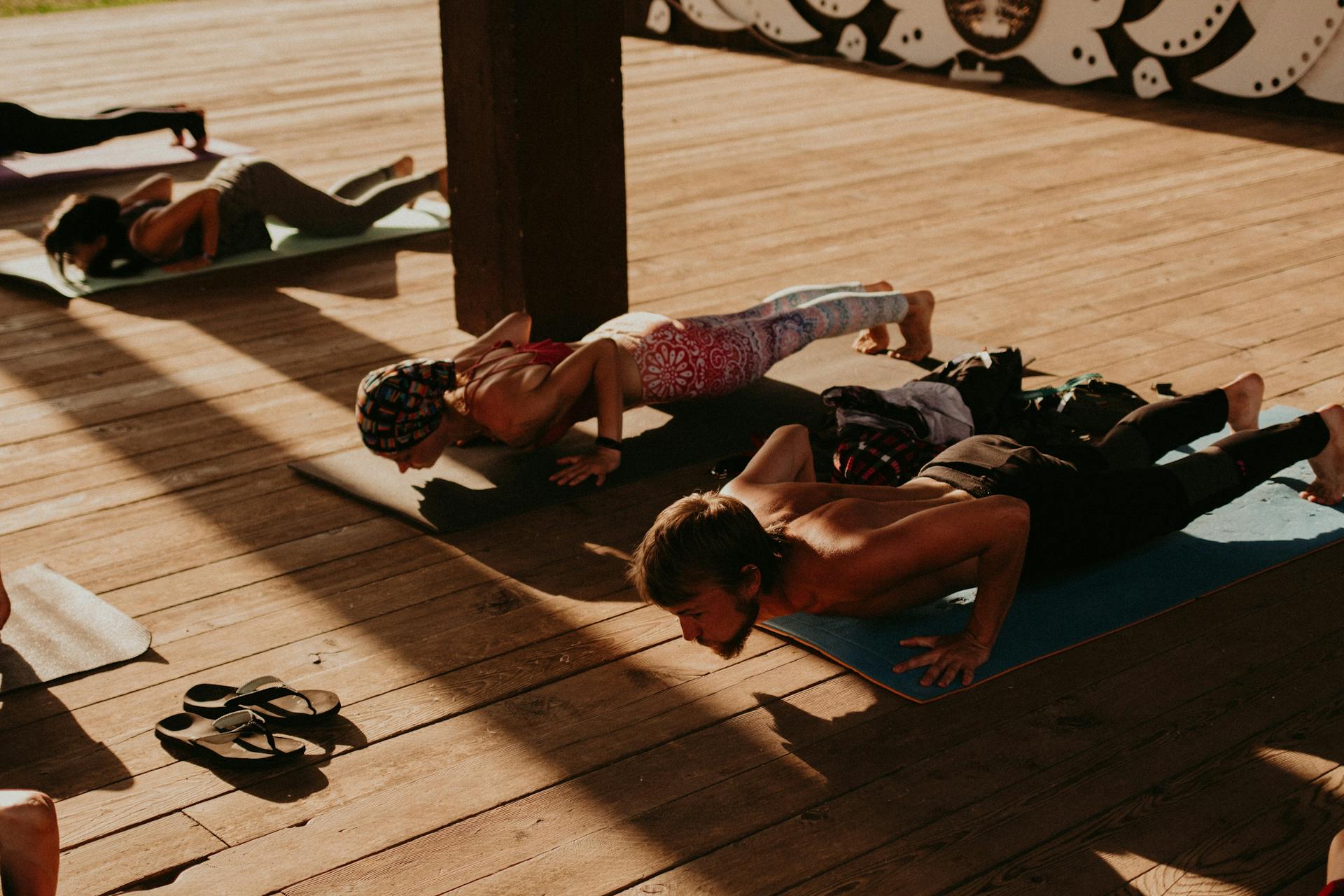 Group of people practicing yoga indoors on wooden floor mats during sunlight.